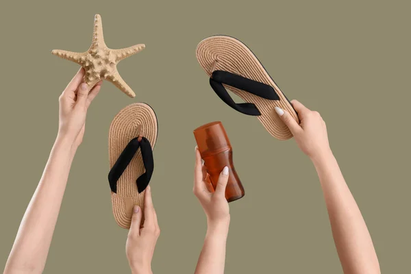 Female hands with bottle of sunscreen cream, flip flops and starfish on green background