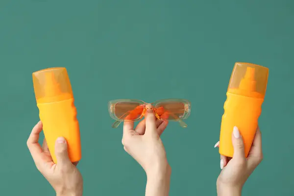 Weibliche Hände Mit Flaschen Sonnencreme Und Sonnenbrille Auf Grünem Hintergrund — Stockfoto