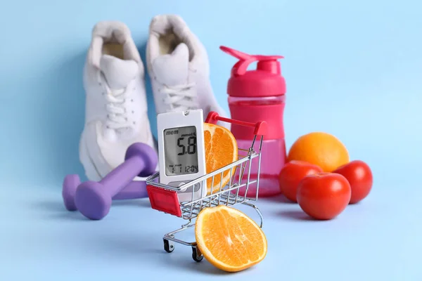 Shopping cart with glucometer, food and sports equipment on blue background. Diabetes concept