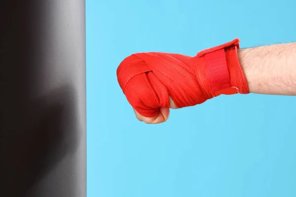 Male hand with red boxing bandage and punch bag on blue background.