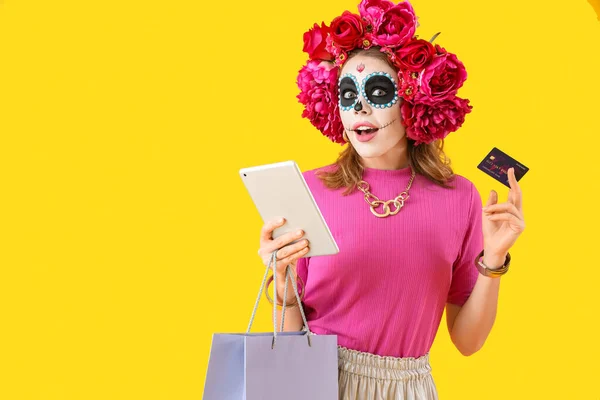 黄色の背景にタブレットコンピュータ クレジットカード ショッピングバッグを持つ若い女性 メキシコの死者の日 ディア ムエルト — ストック写真