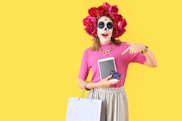 黄色い背景にタブレットコンピュータ クレジットカード ショッピングバッグを指す若い女性を驚かせた メキシコの死者の日 ディア ムエルト — ストック写真
