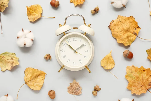 Alarm clock with fallen leaves, acorns and cotton flowers on light background