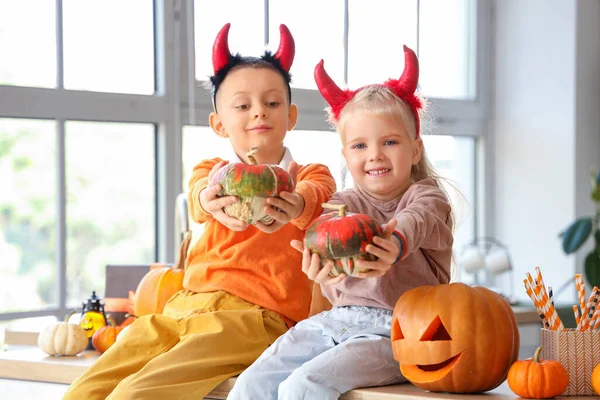 Little children with devil horns and Halloween pumpkins in kitchen