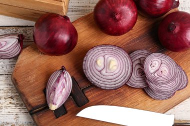 Beyaz ahşap zemin üzerinde taze kırmızı soğan dilimleri olan tahta.