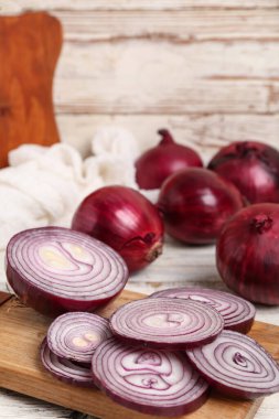 Beyaz ahşap zemin üzerinde taze kırmızı soğan dilimleri olan tahta.