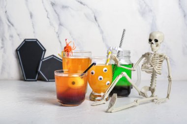 Cadılar bayramı için farklı lezzetli kokteyllerden oluşan bardaklar ve mason kavanozu. Arka planda iskelet var.