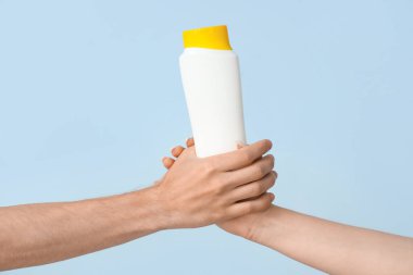 Mavi arka planda güneş kremi şişesi olan kadın elleri.