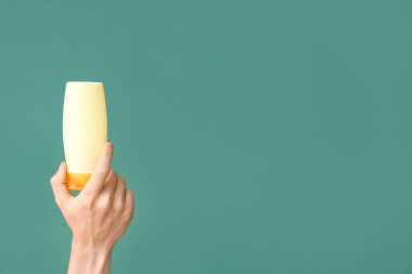 Yeşil arka planda güneş kremi şişesi olan bir kadın el.