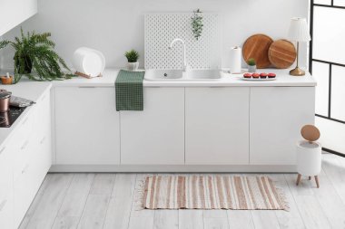 Modern mutfağın içinde şık halı, çöp kutusu ve beyaz tezgahlar var.