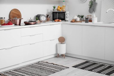 Modern mutfağın içinde şık halı, çöp kutusu ve beyaz tezgahlar var.