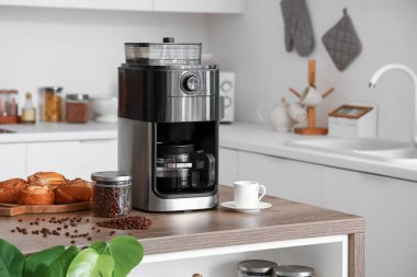 Mutfaktaki kahve makinesinde kavrulmuş fasulye, kahve fincanı ve çörekler.