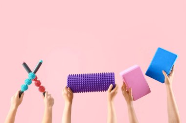 Pembe arka planda farklı masaj ruloları tutan kadın eller.