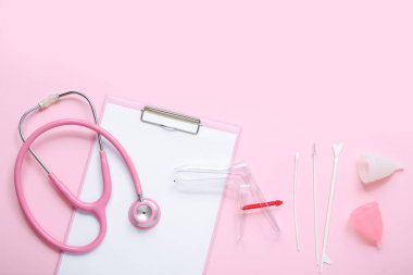 Pembe arka planda jinekolojik spekulum, steteskop, regl bardakları ve pap smear test araçlarıyla pano