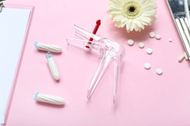 Pembe arka planda jinekolojik spekulum, haplar ve adet tamponları.