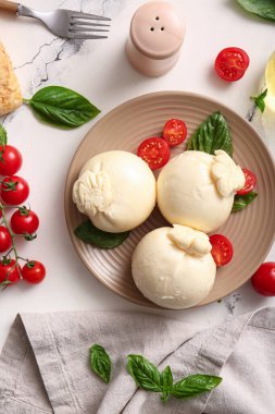 Beyaz arka planda fesleğenli ve domatesli bir tabak lezzetli Burrata peyniri.