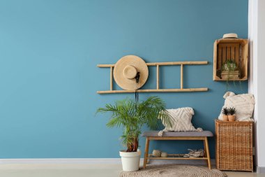 Yastıklı bank, kadın aksesuarları, hasır sepet ve mavi duvarın yanındaki ev bitkileri.
