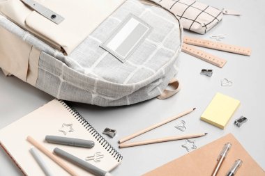 Gri arka planda farklı kırtasiye malzemeleriyle süslü okul çantası.