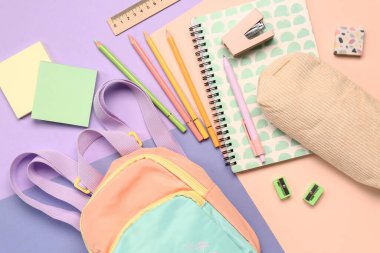 Renkli arka planda farklı kırtasiye malzemesi içeren şık bir okul çantası.