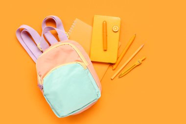 Turuncu arka planda farklı kırtasiye malzemesi içeren şık bir okul çantası.