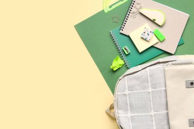 Renkli arka planda farklı kırtasiye malzemesi içeren şık bir okul çantası.