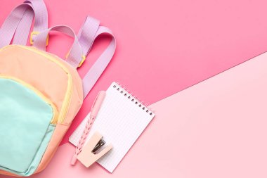 Pembe arka planda farklı kırtasiye malzemesi içeren şık bir okul çantası.