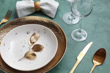 Yeşil masa üzerinde altın yapraklar ve çatal bıçak takımı olan zarif bir masa.