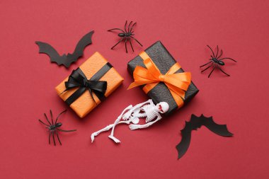 Kırmızı arka planda hediye kutuları ve Cadılar Bayramı süslemeleri olan kompozisyon