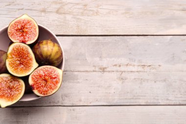 Gri ahşap arka planda taze olgun incirlerle dolu bir kâse.