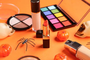 Farklı dekoratif kozmetik ürünleri ve turuncu arka planda Cadılar Bayramı dekorasyonu