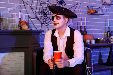 Korsan gibi giyinmiş genç adam Cadılar Bayramı partisinde oturup içki içiyor.