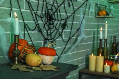 Cadılar Bayramı balkabaklarıyla yanan mum ve karanlık odadaki şömine rafında düşen yapraklar.