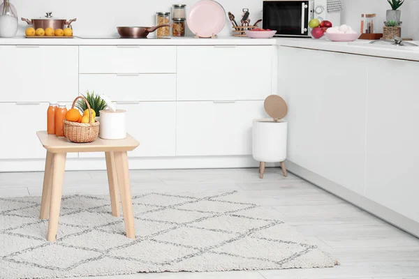 Small table with fruits and juice on stylish rug in modern kitchen