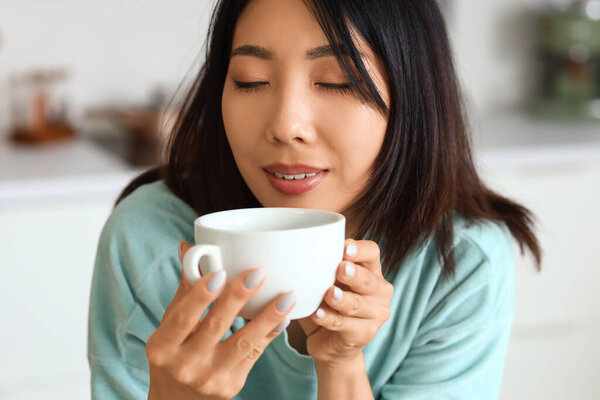 Beautiful Asian woman with cup of hot coffee in kitchen, closeup
