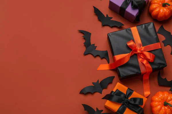 Composition with gift boxes, pumpkins and paper bats for Halloween on brown background