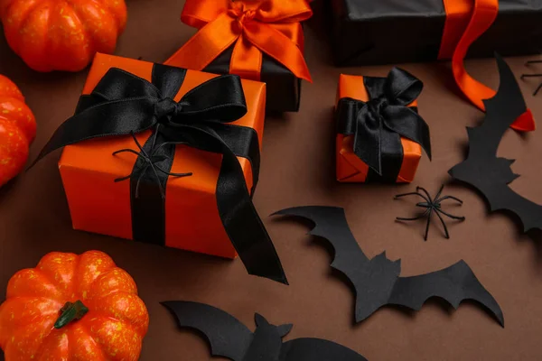 Composition with gift boxes, pumpkins, spiders and paper bats for Halloween on brown background, closeup