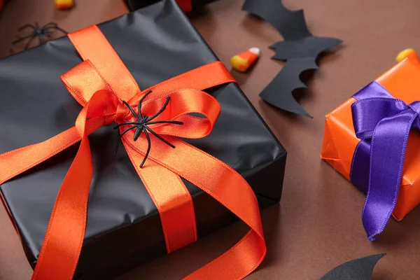 Gift boxes, spider and paper bat for Halloween on brown background, closeup