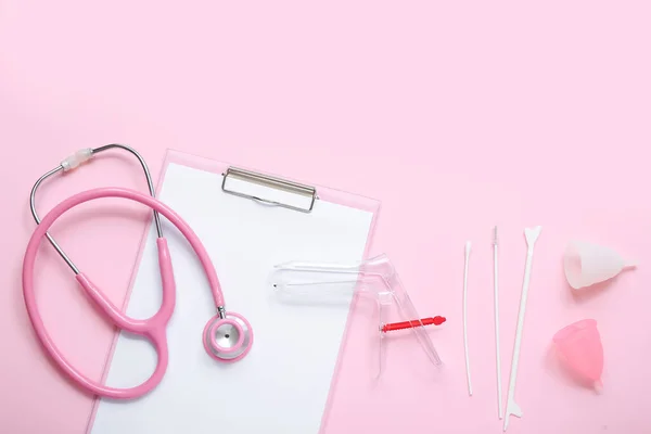 Clipboard with gynecological speculum, stethoscope, menstrual cups and pap smear test tools on pink background