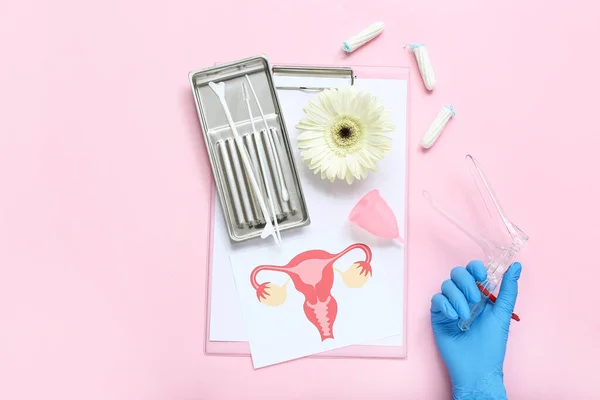 Hand in medical glove, with gynecological speculum, pap smear test tools, drawing of female uterus, menstrual cup and tampons on pink background