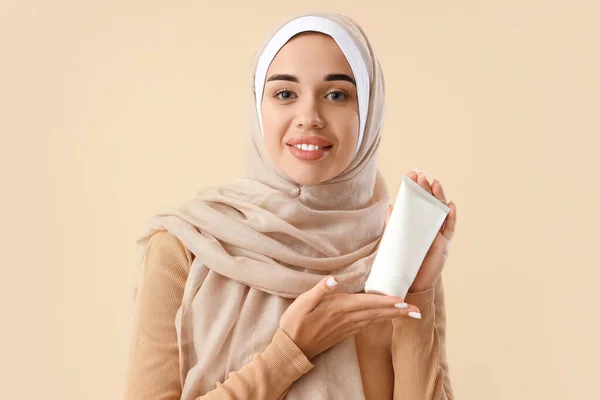 Young Muslim woman with tube of natural cosmetics on light background