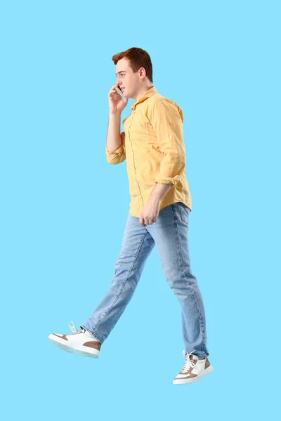 Jumping Młody Człowiek Mówi Przez Telefon Komórkowy Niebieskim Tle — Zdjęcie stockowe