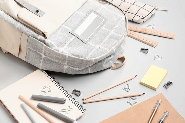 Стильный школьный рюкзак с различными канцтоварами на сером фоне