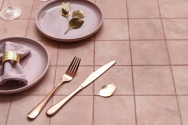 Elegant table setting with golden cutlery on beige tiled background