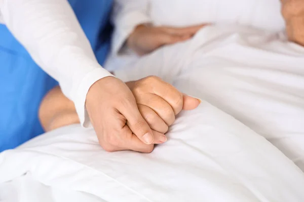 Female nurse holding hand of senior woman in bedroom, closeup