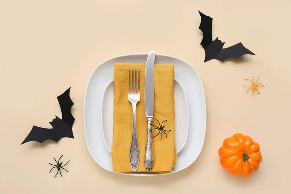 Festive table setting with Halloween bats, spiders and pumpkin on beige background