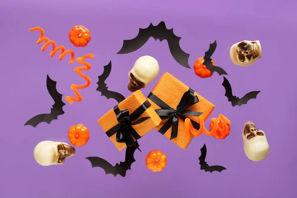 Flying gift boxes, paper bats, pumpkins and skulls for Halloween celebration on purple background