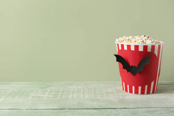 Popcorn bucket with Halloween bats on wooden table against green background