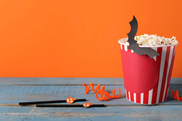 Popcorn bucket with Halloween decor on wooden table against orange background