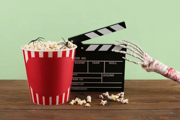 Movie clapperboard and popcorn bucket with Halloween decor on wooden table against green background