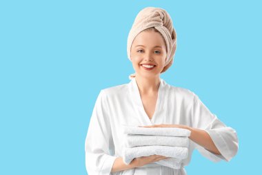 Mavi arka planda temiz yumuşak havluları olan güzel genç bir kadın.